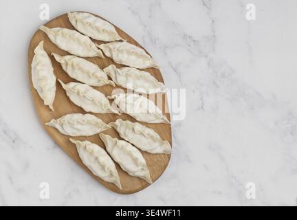 Cibo, gyoza crudi su un asse di legno. Messa a fuoco selettiva, vista dall'alto Foto Stock