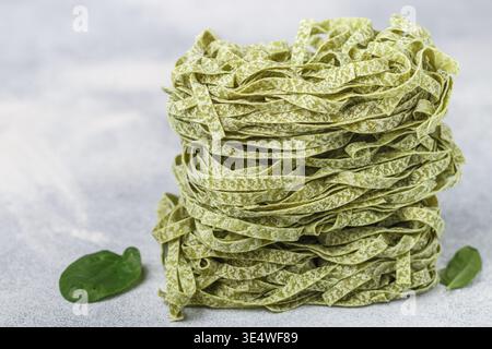 Cibo: Tagliatelle crude fatte in casa di pasta verde italiana con primi piani di spinaci. Spaghetti secchi. Messa a fuoco selettiva, copia spazio Foto Stock