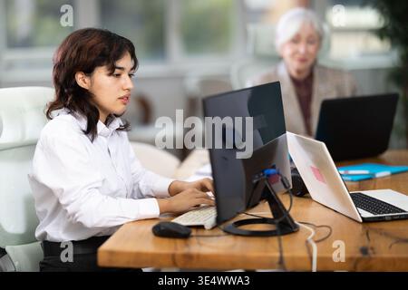 Giovane donna seduta alla scrivania e a scrivere su un computer portatile in un ufficio moderno Foto Stock