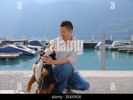 L'uomo asiatico si accosta per accarezzare un cane da montagna bernese in un lago in Svizzera Foto Stock
