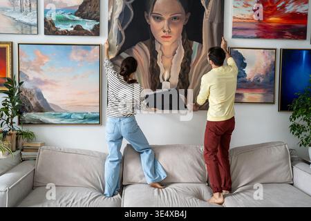 La coppia di pittori in casa studio appende opere d'arte sul muro. Guy Girl insieme fanno la composizione delle immagini Foto Stock