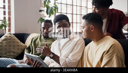 Parlare, uomini e tablet per risultati di calcio, Internet e live streaming per notizie sportive. Rilassati, persone e amici a casa, discussione e tecnologia per Foto Stock