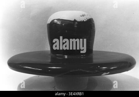 Sloviansk, anni '1960, armature-Insulator Plant (AIZ) - Una vista del profilo laterale di un isolante ceramico difettoso ad alta tensione che presenta un'applicazione gravemente irregolare di smalto scuro. L'immagine di archivio cattura le gocce spesse e irregolari del rivestimento contro la base in porcellana bianca grezza, evidenziando un evidente fallimento nel processo di immersione. Questa straordinaria macro fotografia documenta le rigide realtà di controllo della qualità della produzione sovietica della metà del secolo, preservando la storia dell'industria pesante nel pacifico Donbas. Foto Stock