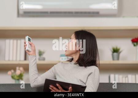 Donna che regola l'aria condizionata con telecomando Foto Stock