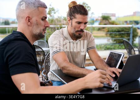 Due uomini che collaborano all'aperto utilizzando un notebook e un tablet Foto Stock