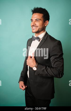 Uomo sorridente che indossa un papillon e una tuta sullo sfondo color ottanio Foto Stock