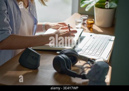 Donna che scrive su un notebook accanto a un computer portatile sulla scrivania dell'ufficio domestico. Concetto di prendere appunti e di routine di lavoro a distanza Foto Stock