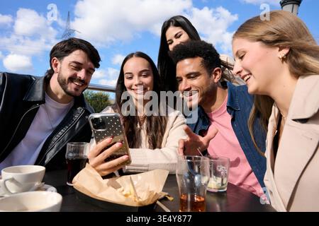 Diversi amici ridono e condividono contenuti su smartphone Foto Stock