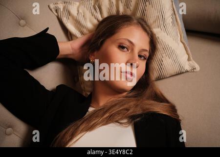 Giovane donna che si rilassa sul divano guardando la macchina fotografica Foto Stock