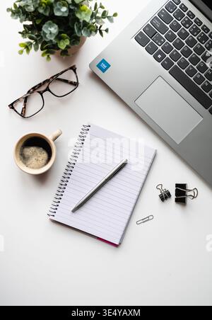 Vista dall'alto della scena di lavoro con computer, caffè, blocco note su un tavolo bianco. Foto Stock
