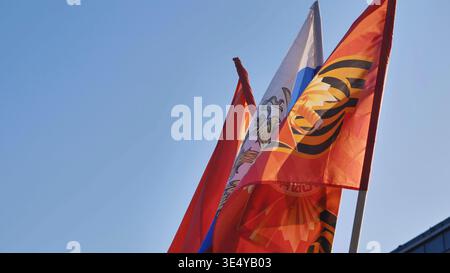 Bandiere nazionali russe e del nastro di San Giorgio che battono simboli patriottici contro il cielo blu Foto Stock
