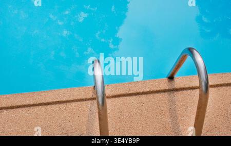 Vista orizzontale della piscina del resort con maniglie a scala metalliche sulla destra. L'acqua blu brillante riempie il lato sinistro della cornice, cre Foto Stock