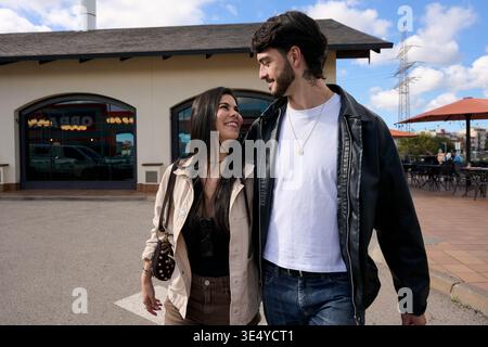 Giovane coppia che cammina e sorride insieme in un ambiente urbano Foto Stock