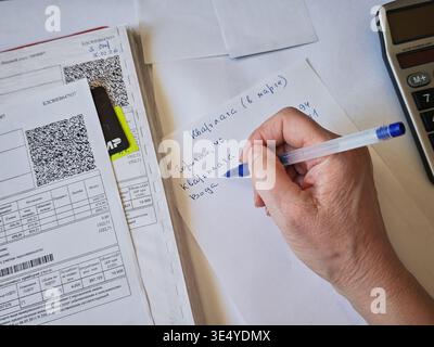 Kirov, Russia - 18 marzo 2026: Una persona scrive le spese mensili durante l'organizzazione di bollette e ricevute a un tavolo con una calcolatrice nelle vicinanze. Foto Stock