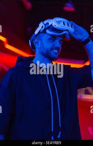 Uomo alla moda e alla moda che indossa occhiali VR in una stanza buia con luce al neon. Realtà virtuale Foto Stock