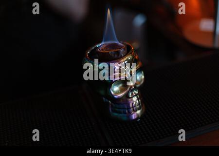 Bellissimo vetro cromato con cocktail alcolici con mango e fuoco sul bancone del bar Foto Stock