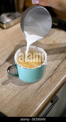 Il barista versa il latte creando una latte art nella tazza da caffè. Foto Stock