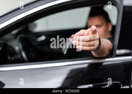 Il manager uomo felice e figo si siede in macchina e tiene le chiavi della macchina. Consegna le chiavi, noleggio auto e acquisto Foto Stock