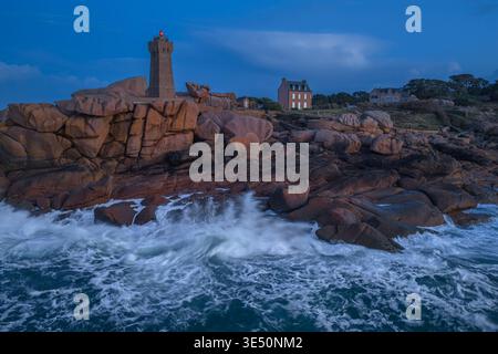 Veduta aerea del faro di Ploumanaca'h in piedi su rocce di granito rosa con onde che si infrangono durante l'ora blu a Perros-Guirec, Bretagne, Francia. Foto Stock