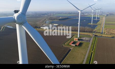 Vista aerea di alte turbine eoliche bianche e di una grande fattoria a pannelli solari integrata in un paesaggio agricolo pianeggiante con canali di irrigazione e cu Foto Stock