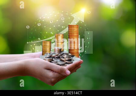 Primo piano di mani che detengono monete d'oro impilate con grafico di crescita e rete globale su sfondo bokeh verde. Foto Stock