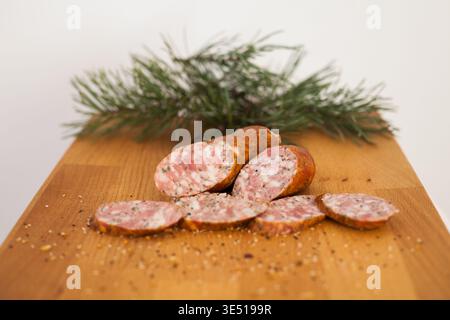 La tradizionale salsiccia polacca del cacciatore affumicato (mysliwska) tagliata su un asse di legno con un ramo di abete rosso, isolata su sfondo bianco. Foto Stock