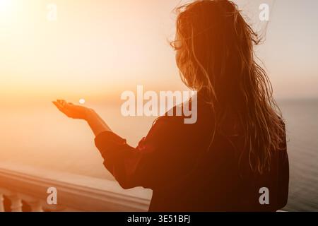 Donna tramonto oceano che guarda all'orizzonte mentre tiene il sole in mano all'ora d'oro con spazio copia Foto Stock