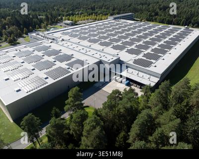 I pannelli solari coprono il tetto di un grande edificio in un'area boschiva, sostenendo la produzione di energia rinnovabile per un futuro più pulito. Foto Stock