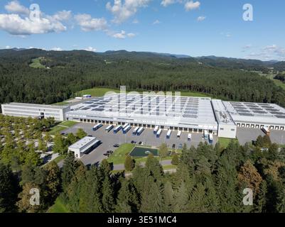 Questa vista aerea mostra un centro logistico con magazzini, banchine di carico e camion circondati da alberi e colline. Foto Stock