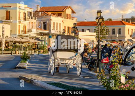 Una carrozza trainata da cavalli percorre la strada principale di negozi e caffetterie sul mare dello storico porto di Egina, sull'isola di Egina, in Grecia. Foto Stock
