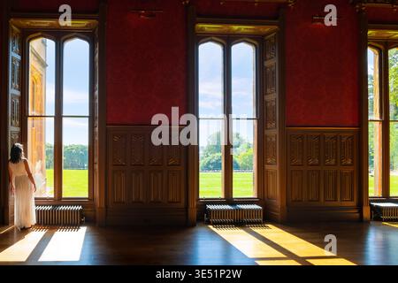 Una donna sta alla luce del sole guardando fuori da una finestra all'interno della sala del castello di Lews, affacciata su un prato e un giardino a Stornoway, in Scozia. Foto Stock