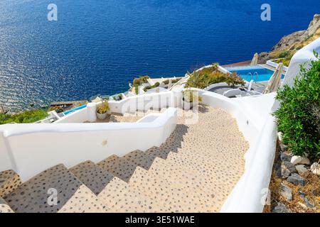 Una ripida scala si snoda verso il basso verso terrazze imbiancate a calce con resort e piscine nel villaggio di Oia, in Grecia, sull'isola greca di Santorini. Foto Stock