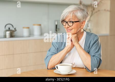 Buon giorno. Comfort rilassato anziano anziano anziano anziano donna nonna che beve bevande calde tè e caffè in cucina a casa. Donna matura che riposa goditi la calma mattinata nella casa moderna da sola. Concetto di pensione Foto Stock