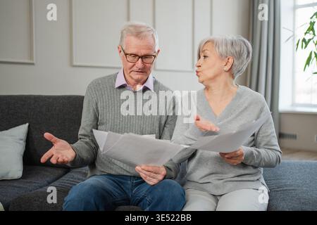 Triste stanco, deluso, coppia di anziani di mezza età siedono con un documento cartaceo. Infelice anziano maturo donna che legge banconote che gestiscono le finanze bancarie calcolano le tasse pianificazione prestito pagamento pensione Foto Stock