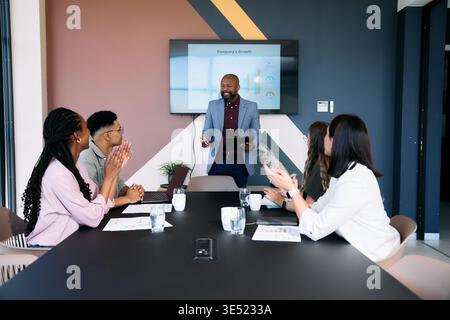 Uomo d'affari maturo e fiducioso che presenta la crescita dell'azienda mentre diversi team applaudono in sala riunioni Foto Stock