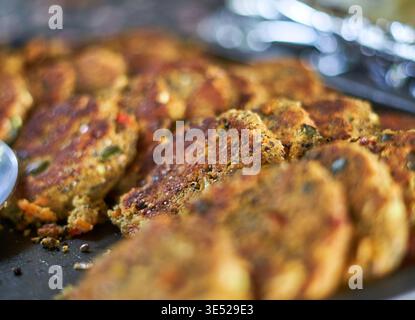 Primo piano di polpettine o frittelle di verdure dorate disposte su una teglia da forno scura o su una superficie di cottura. Le polpette sono croccanti e ruvide Foto Stock