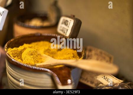 Foto ravvicinata di un contenitore in ceramica riempito di polvere di curry giallo brillante. Un cucchiaio di legno poggia sopra la spezia, parzialmente sommersa Foto Stock