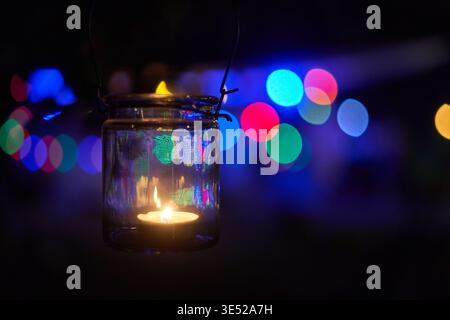 Una fotografia ravvicinata di una candela illuminata che brucia all'interno di una lanterna in vetro trasparente con coperchio a chiusura metallica e manico in filo, sospeso nel Foto Stock