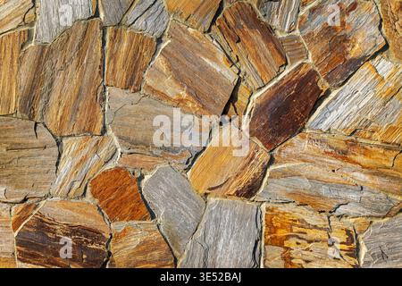 Pareti in pietra naturale dai toni caldi. Primo piano di una parete irregolare in pietra naturale con tonalità grigie e ruggine, ideale per ricerche su muratura Foto Stock