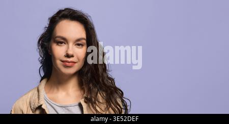 Giovane donna in piedi e guarda la fotocamera con sfondo viola chiaro durante il giorno Foto Stock