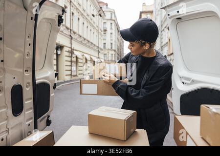 Donna in uniforme che tiene i pacchi mentre si trova davanti al bagagliaio dell'auto. Corriere che prepara i pacchi per la consegna Foto Stock