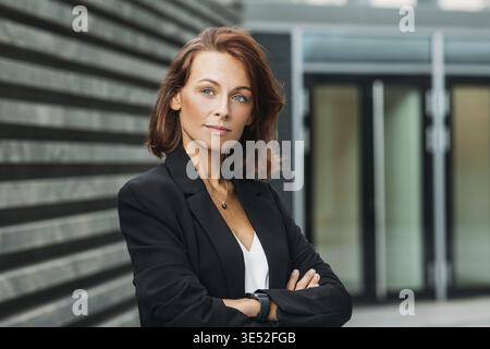 Ritratto di una donna d'affari sicura di sé con i capelli di zenzero. Donna d'affari di mezza età in piedi con le braccia incrociate all'aperto Foto Stock