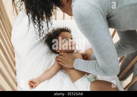 Donna appoggiata a una culla. Giovane madre che guarda suo figlio e si tiene per mano Foto Stock