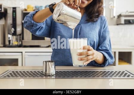 Primo piano di una barista che versa il latte dalla manomissione in un bicchiere Foto Stock