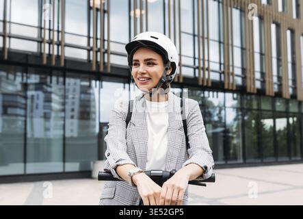Bella donna sorridente che indossa il casco da ciclismo guardando lontano mentre si trova in città Foto Stock