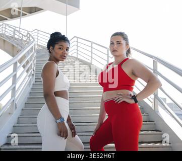 Due donne in abbigliamento sportivo con colori diversi che si posizionano insieme su una scala all'aperto Foto Stock