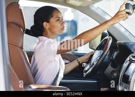 Vista laterale della donna regolazione dello specchietto retrovisore mentre si è alla guida di un veicolo Foto Stock