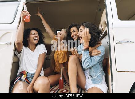 Gruppo multietnico di donne che frequentano il viaggio. Amici nel furgone che alzano le mani e ridono Foto Stock