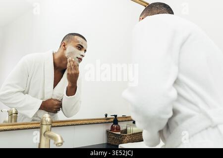 Uomo bello applicando un argilla naturale maschera per il viso in bagno Foto Stock