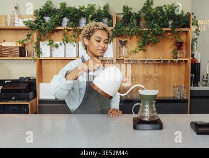 Giovane barista femminile con capelli corti preparare il caffè con un filtro al bancone Foto Stock